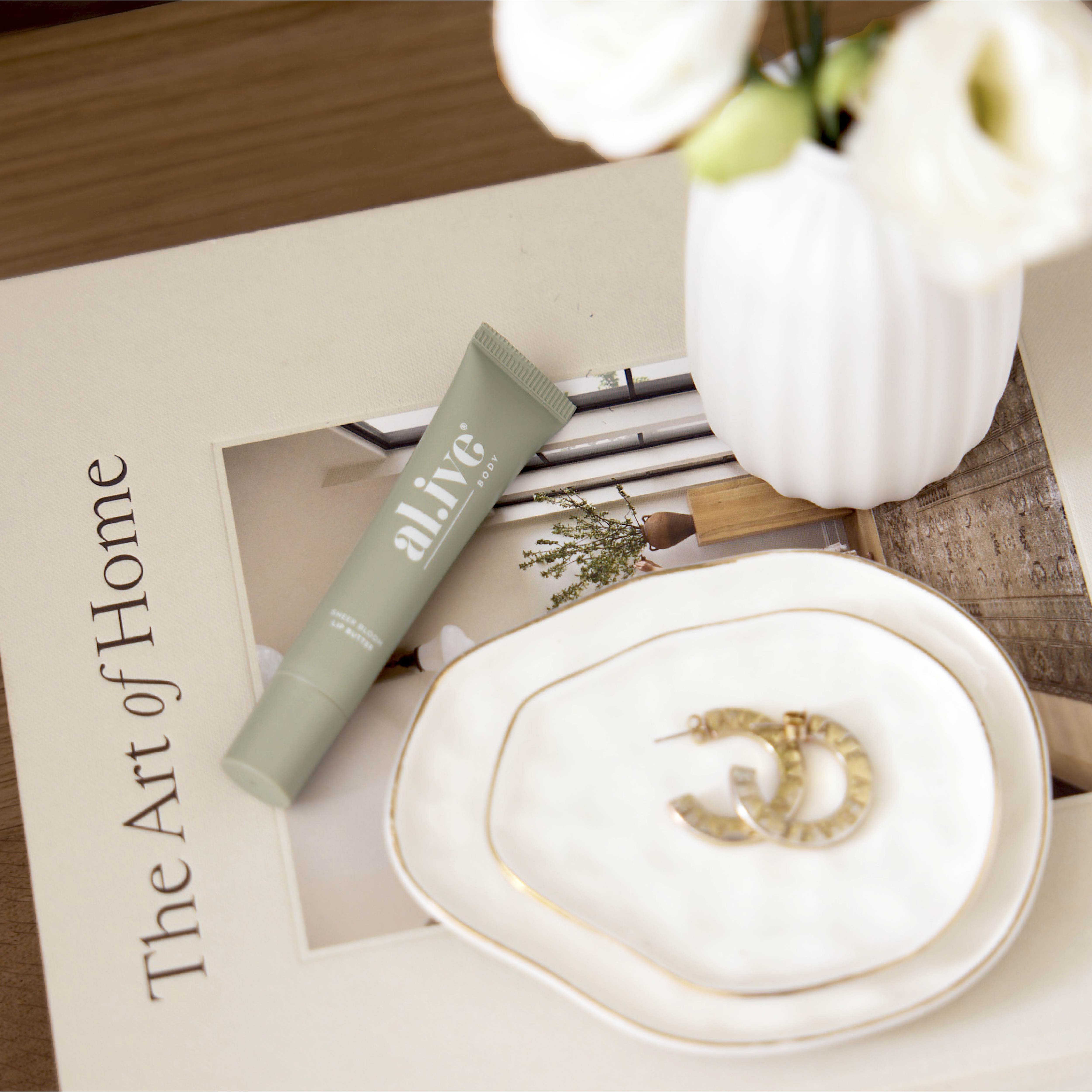 Jewelry dish with ring, tube of lip balm, and magazine on a wooden surface