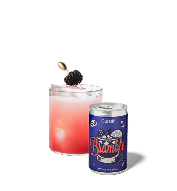 Cocktail with a blackberry garnish next to a can of Curatif Bramble on a white background