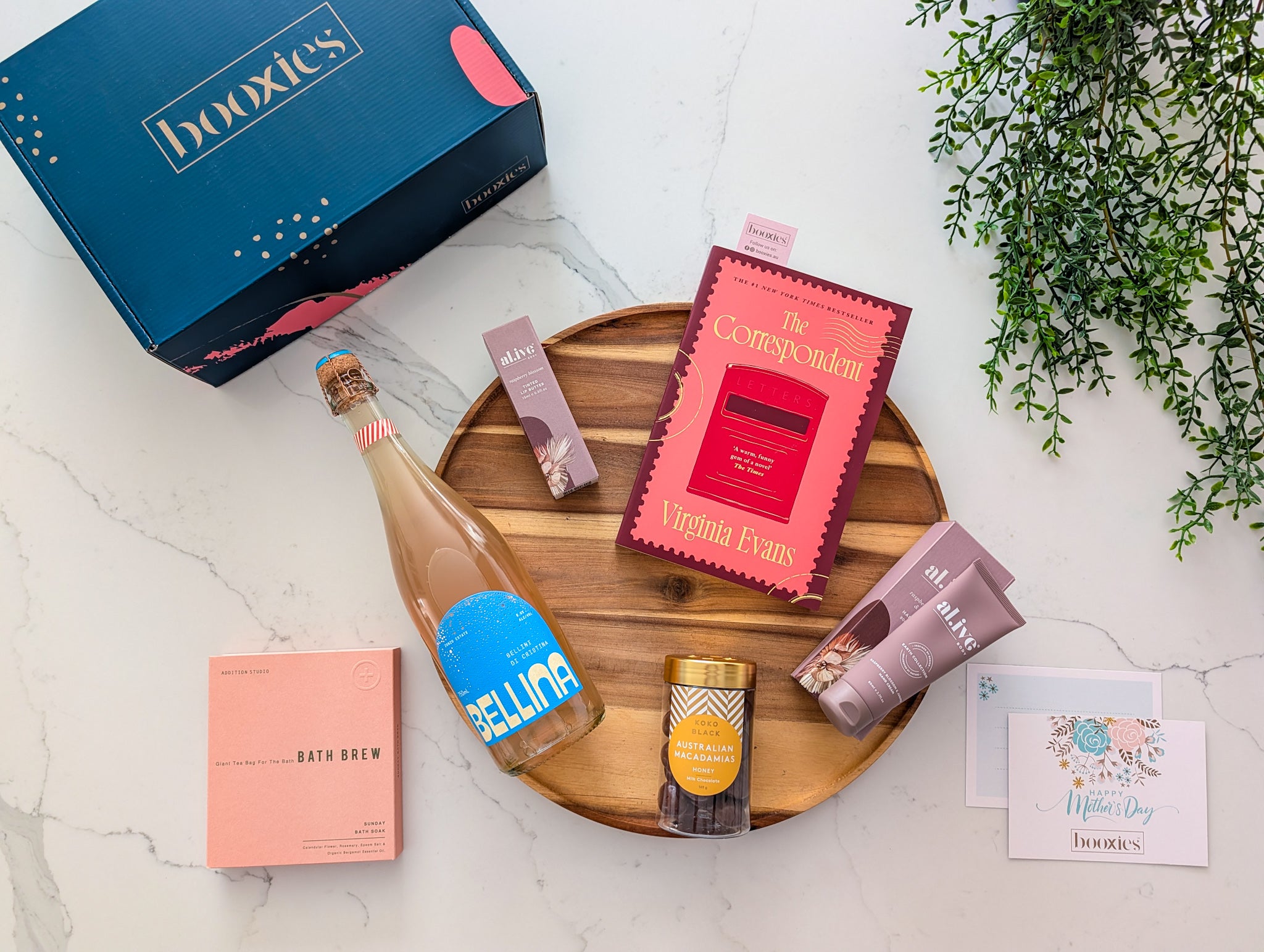 Gourmet gift set with Bellina Spritz from Zonzo, chocolate from koko black, alive hand cream and lip butter and bath brew from addition studio and a book on a wooden tray making mother's day gift box from booxies